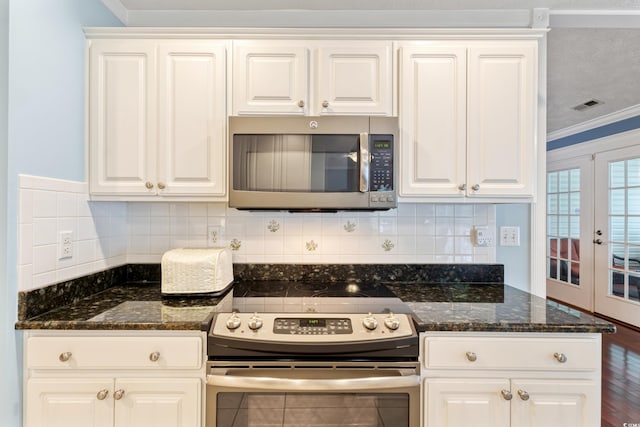 kitchen with appliances with stainless steel finishes, ornamental molding, white cabinetry, dark stone counters, and backsplash