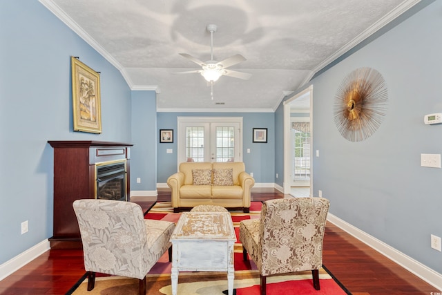 living area featuring wood finished floors, ceiling fan, ornamental molding, baseboards, and a glass covered fireplace