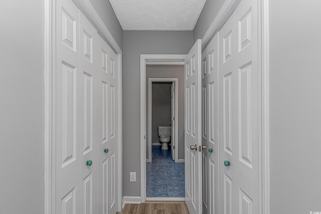 hall with wood finished floors, a textured ceiling, and baseboards
