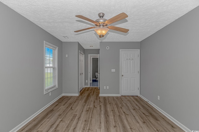 unfurnished bedroom featuring light wood-style flooring, a textured ceiling, baseboards, and ceiling fan