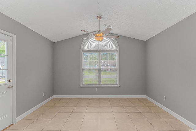 unfurnished room with ceiling fan, vaulted ceiling, a textured ceiling, baseboards, and light tile patterned floors