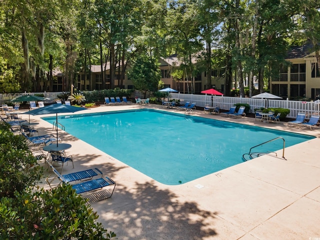 community pool featuring fence, a patio, and view of wooded area