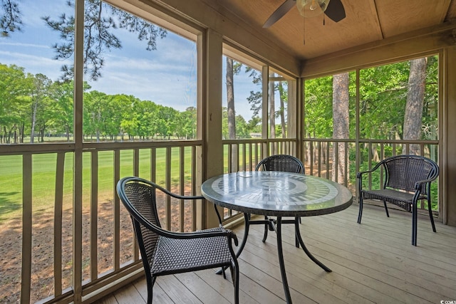 sunroom / solarium with ceiling fan, outdoor dining area, and view of wooded area