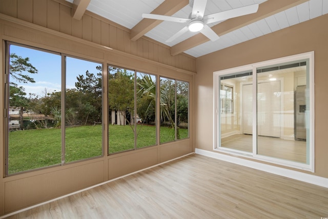 unfurnished sunroom featuring ceiling fan, beamed ceiling, wood finished floors, and baseboards