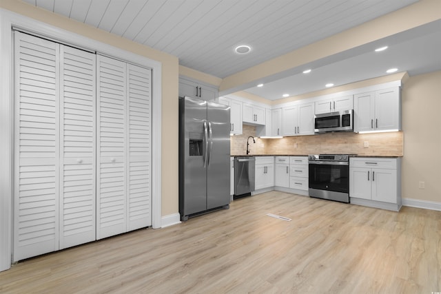 kitchen with appliances with stainless steel finishes, decorative backsplash, light wood finished floors, a sink, and baseboards