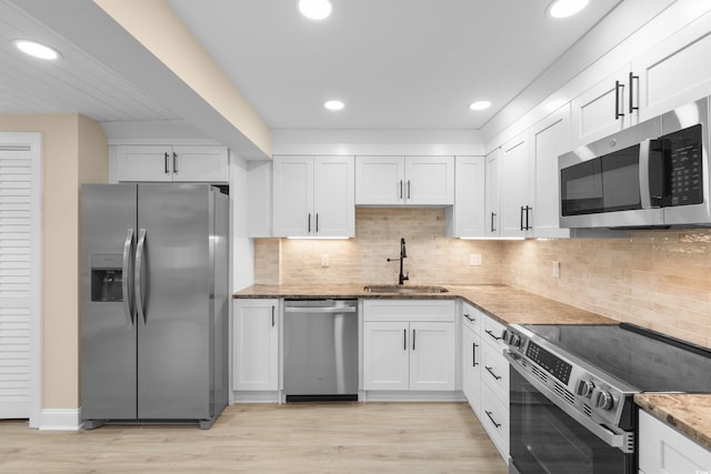 kitchen with appliances with stainless steel finishes, a sink, white cabinets, light stone countertops, and recessed lighting