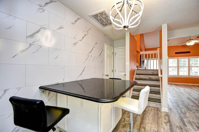 990 Palisade Cir, Myrtle Beach, SC 29577 - kitchen featuring a textured ceiling, a kitchen breakfast bar, dark countertops, a chandelier, and wood finished floors
