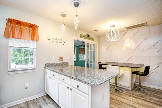990 Palisade Cir, Myrtle Beach, SC 29577 - kitchen featuring a peninsula, white cabinetry, a textured ceiling, light wood finished floors, and decorative light fixtures