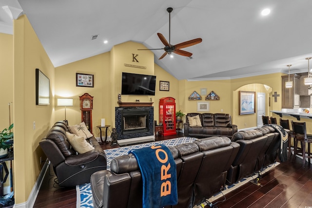 living area featuring ceiling fan, dark wood-type flooring, arched walkways, a fireplace, and vaulted ceiling