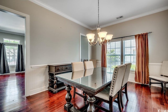 dining room with a chandelier, crown molding, dark wood-type flooring, a wainscoted wall, and baseboards