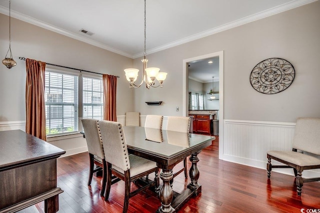 dining area featuring a chandelier, crown molding, a wainscoted wall, and dark wood-style flooring