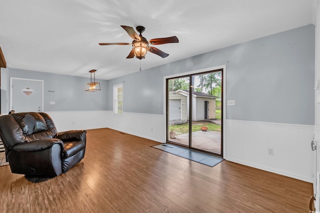 living room with a wainscoted wall, wood finished floors, and a ceiling fan