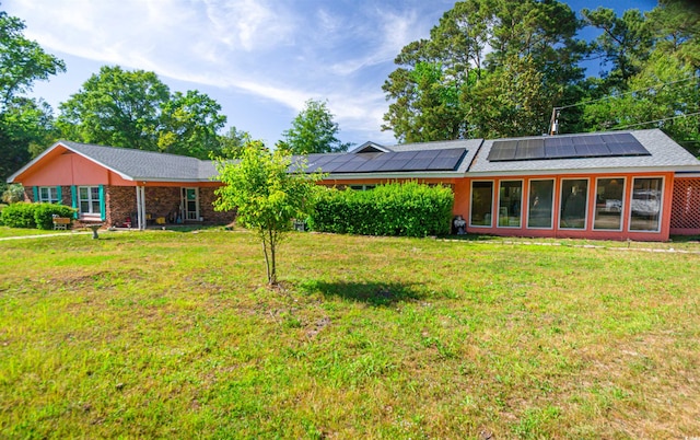 rear view of property featuring roof mounted solar panels and a lawn