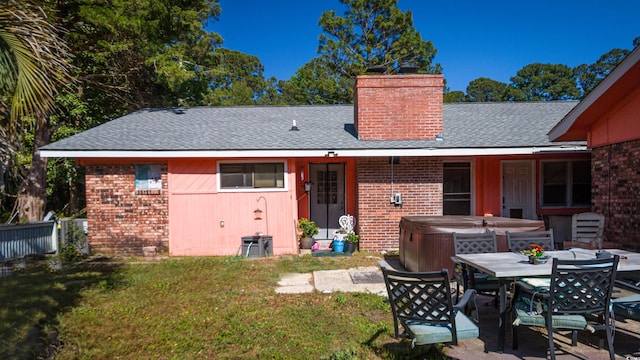 back of house with a hot tub, brick siding, roof with shingles, and a chimney