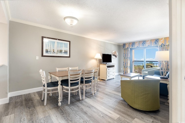 dining space featuring a textured ceiling, ornamental molding, baseboards, and wood finished floors