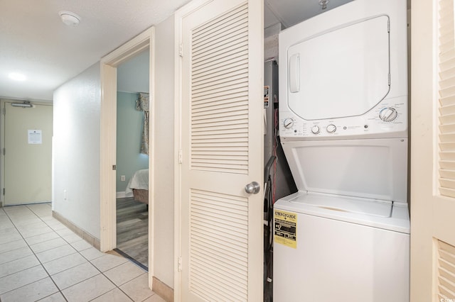 laundry area featuring stacked washer / dryer, light tile patterned floors, and baseboards