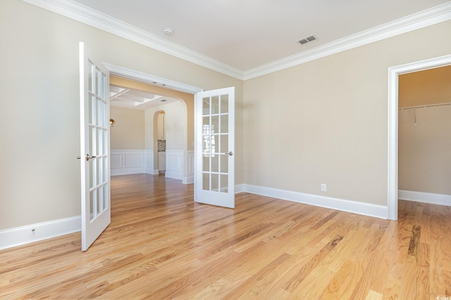 empty room with french doors, arched walkways, crown molding, and light wood-style flooring