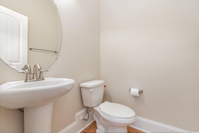half bathroom featuring baseboards, toilet, wood finished floors, and a sink