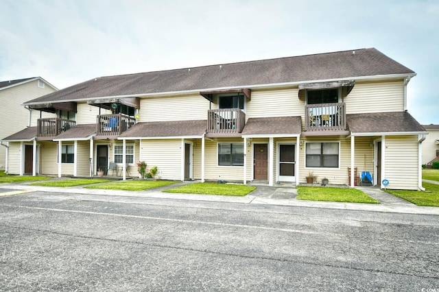 townhome / multi-family property featuring a balcony, roof with shingles, and a front lawn