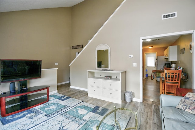 living area featuring wood finished floors, high vaulted ceiling, baseboards, and stairs