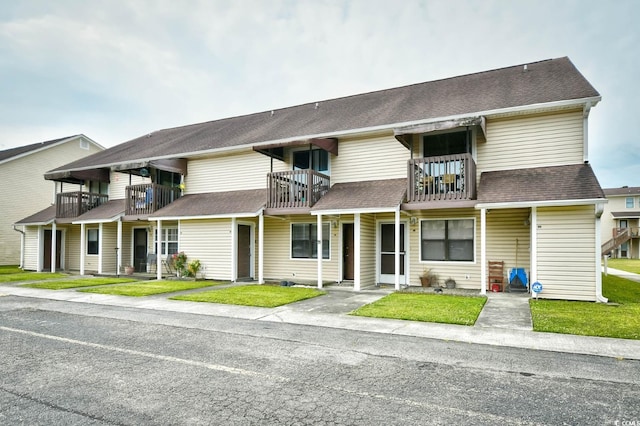 multi unit property featuring a balcony, a front yard, and a shingled roof
