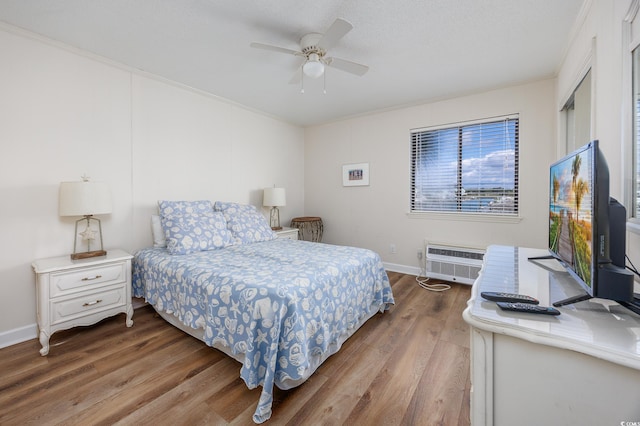 bedroom featuring wood finished floors, a wall unit AC, ornamental molding, baseboards, and ceiling fan