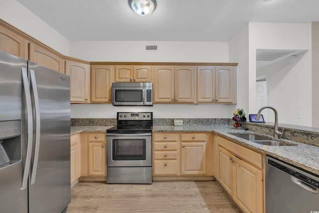 kitchen with stainless steel appliances, a sink, light brown cabinets, light stone counters, and a textured ceiling