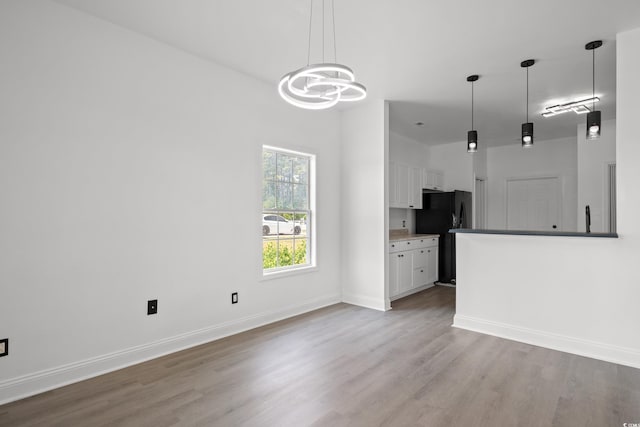unfurnished living room featuring wood finished floors, a chandelier, and baseboards