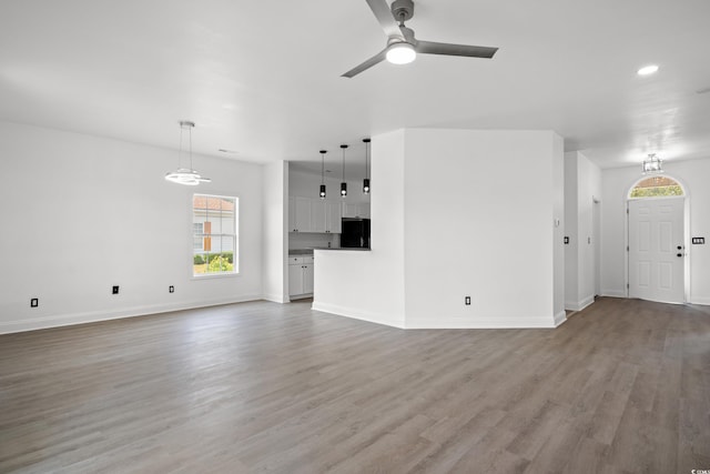 unfurnished living room with healthy amount of natural light, light wood-style flooring, a ceiling fan, baseboards, and recessed lighting