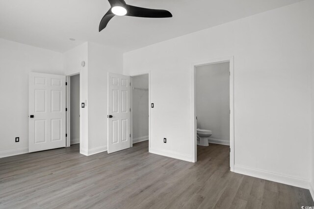 unfurnished bedroom featuring wood finished floors, ensuite bathroom, and baseboards