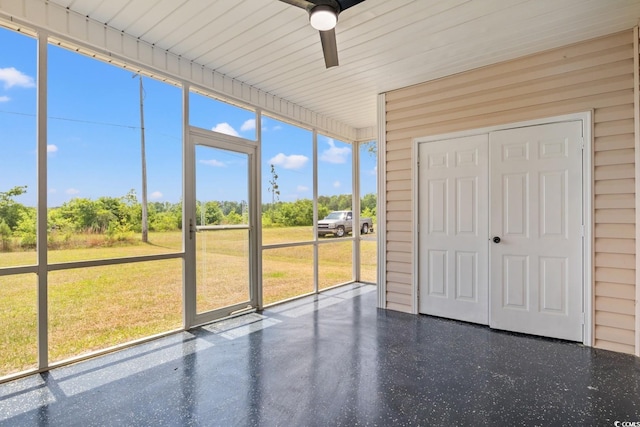 unfurnished sunroom with ceiling fan and view of wooded area