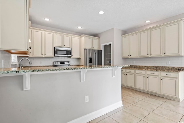 kitchen with appliances with stainless steel finishes, cream cabinetry, dark stone countertops, and recessed lighting
