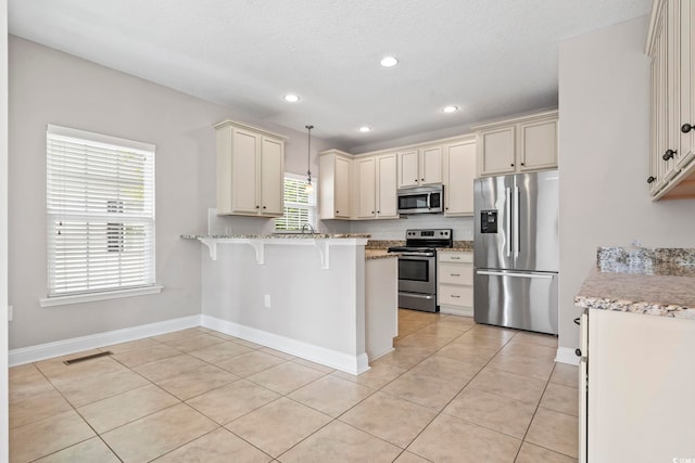 kitchen featuring stainless steel appliances, a kitchen bar, cream cabinets, a peninsula, and light tile patterned floors