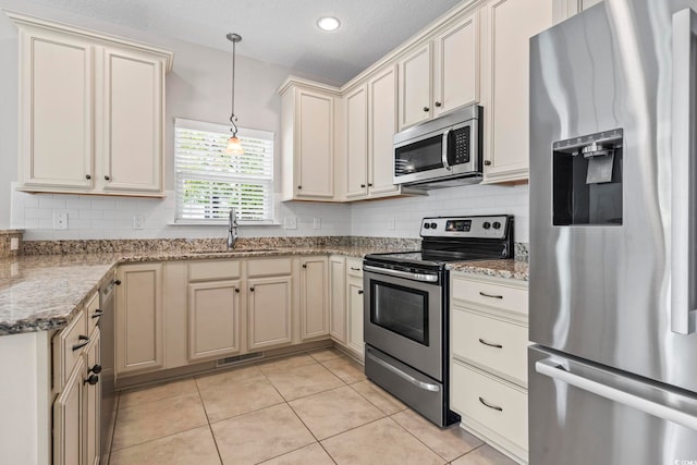 kitchen featuring appliances with stainless steel finishes, a sink, tasteful backsplash, light tile patterned flooring, and pendant lighting