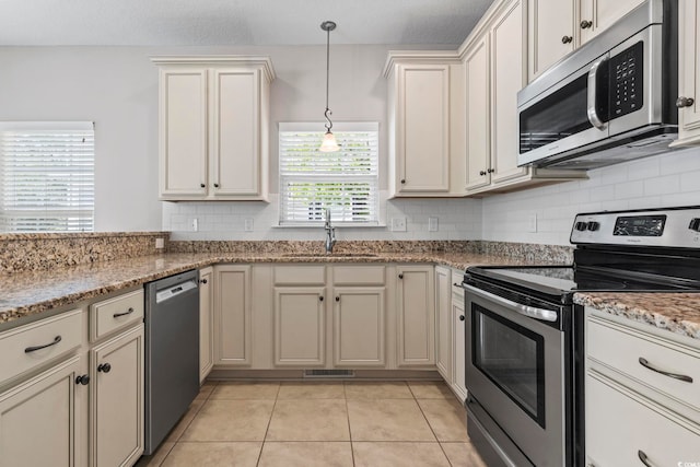 kitchen featuring appliances with stainless steel finishes, a sink, backsplash, light tile patterned floors, and hanging light fixtures