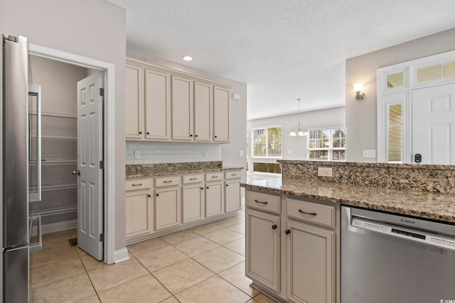 kitchen with appliances with stainless steel finishes, cream cabinetry, light tile patterned flooring, backsplash, and a textured ceiling