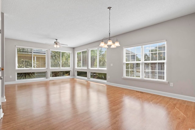 unfurnished dining area featuring a textured ceiling, baseboards, wood finished floors, a ceiling fan, and a chandelier