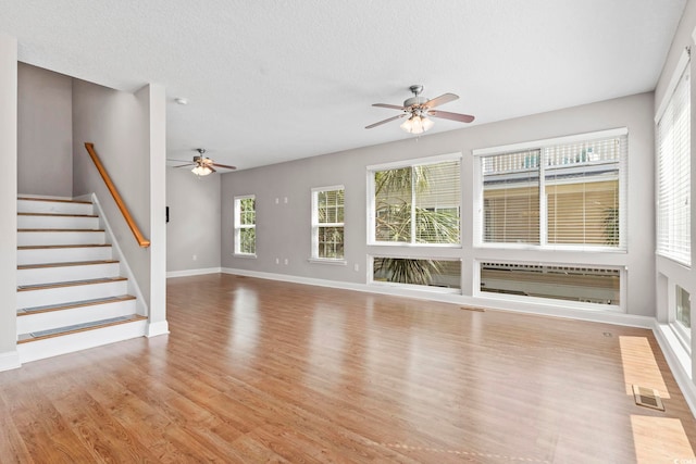 unfurnished living room featuring ceiling fan, wood finished floors, baseboards, stairs, and a textured ceiling
