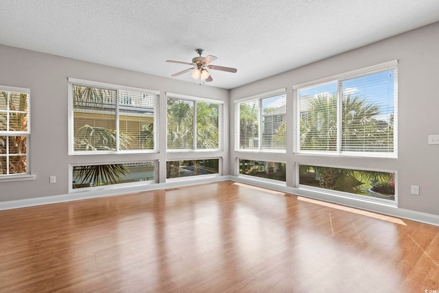 unfurnished sunroom with wood finished floors, a textured ceiling, and baseboards