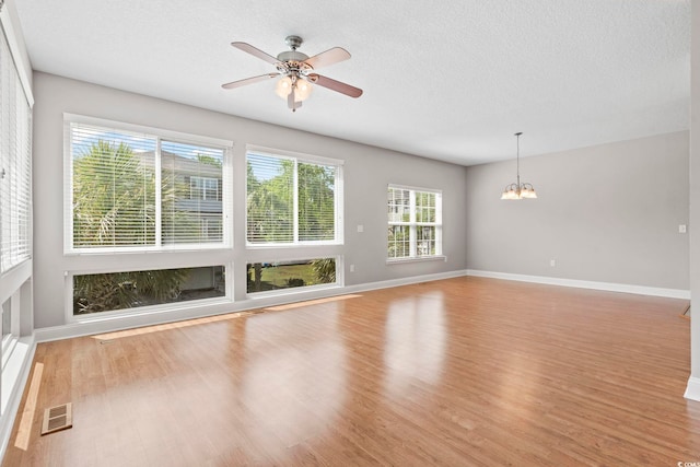 empty room with a chandelier, ceiling fan, light wood-style floors, baseboards, and a textured ceiling