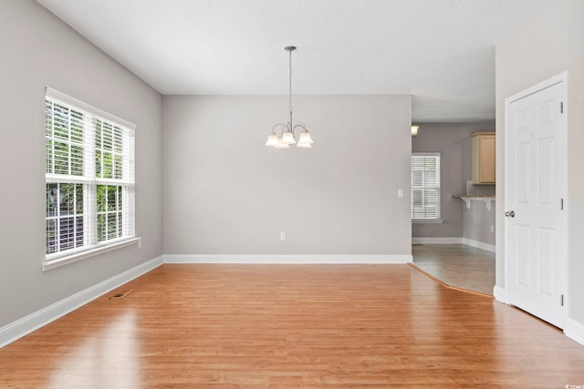 unfurnished room featuring light wood-style floors, a chandelier, and baseboards