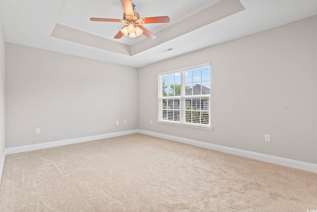 empty room featuring a raised ceiling, baseboards, and carpet flooring