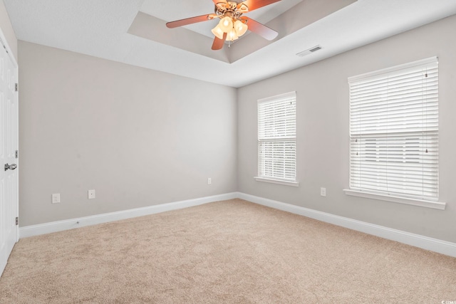 carpeted empty room with ceiling fan, baseboards, and a tray ceiling