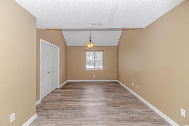 unfurnished room featuring light wood-style floors, baseboards, lofted ceiling, and a textured ceiling