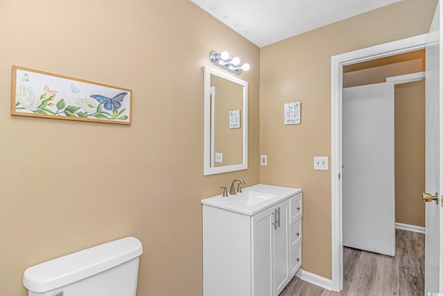 half bathroom with wood finished floors, toilet, vanity, and baseboards