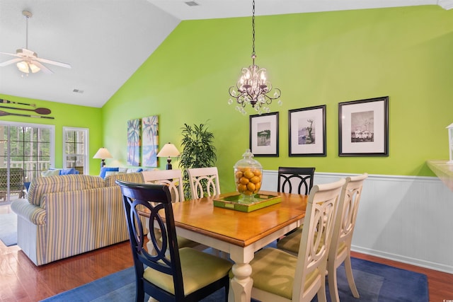 dining space with wainscoting, ceiling fan, wood finished floors, a chandelier, and high vaulted ceiling