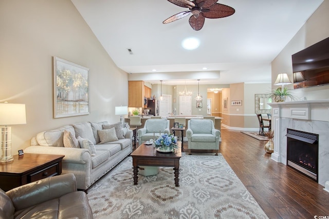 living area with ceiling fan, wood finished floors, baseboards, vaulted ceiling, and a chandelier