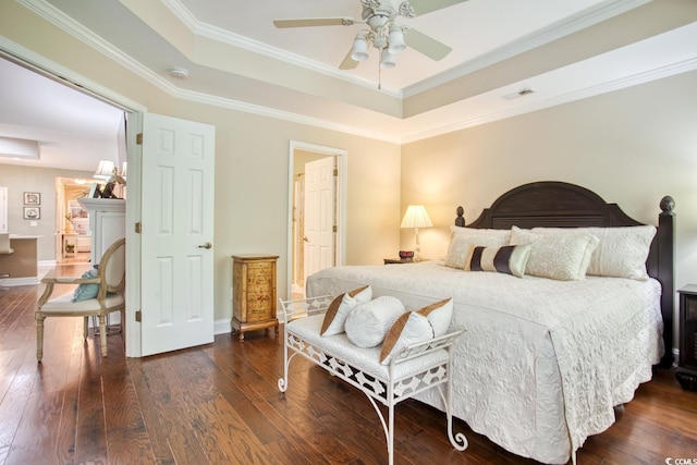 bedroom featuring a tray ceiling, dark wood-style flooring, crown molding, baseboards, and a ceiling fan