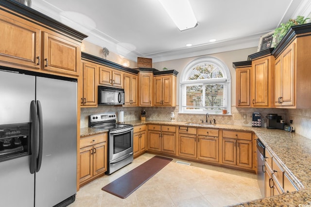 kitchen featuring appliances with stainless steel finishes, a sink, brown cabinets, ornamental molding, and tasteful backsplash