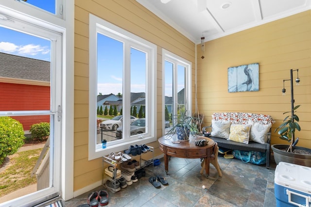 sunroom / solarium featuring healthy amount of natural light, wooden walls, stone finish floors, and crown molding